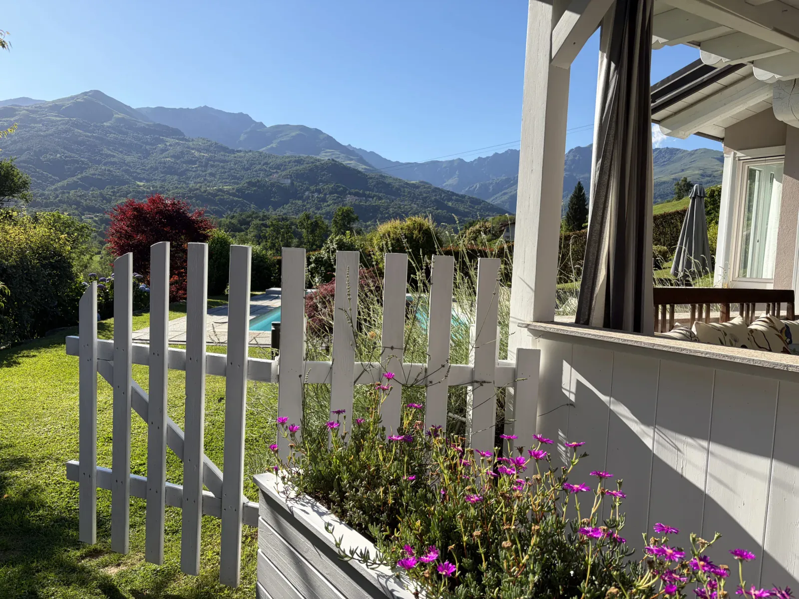Vista sulle montagne dal portico, tra staccionata bianca e fiori