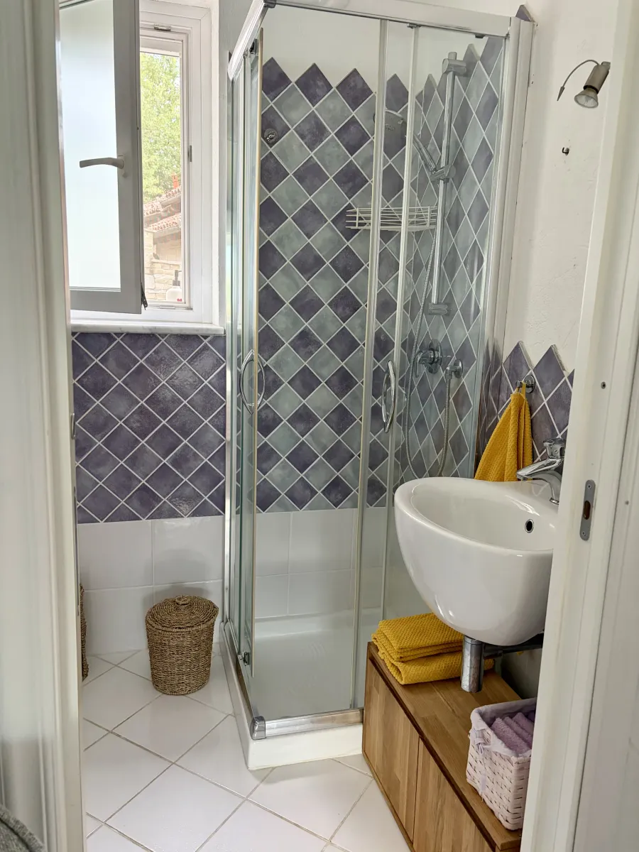 Bagno luminoso con doccia, piastrelle a rombi e dettagli color senape