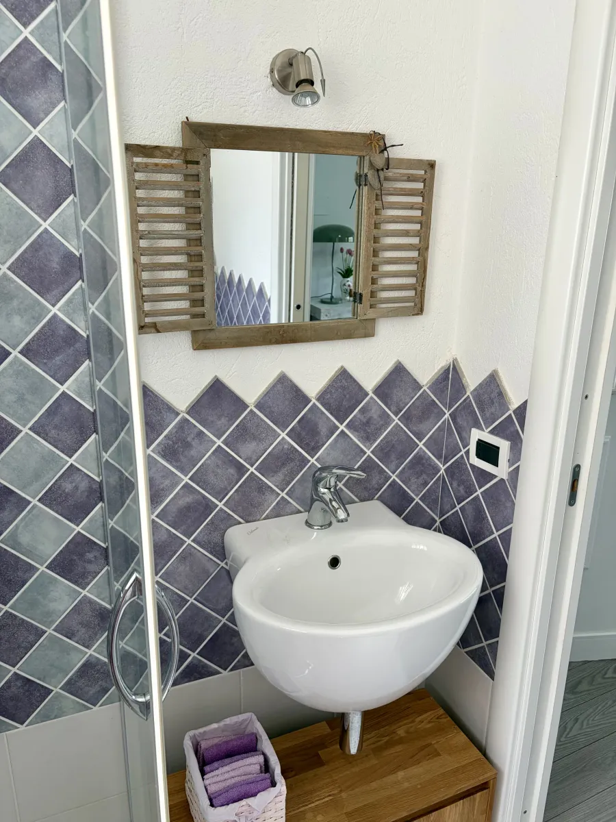 Lavabo del bagno con piastrelle viola a rombi e specchio con ante in legno